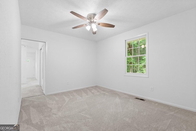 empty room featuring a textured ceiling, ceiling fan, carpet flooring, and visible vents