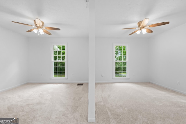 carpeted empty room featuring a healthy amount of sunlight, visible vents, and a ceiling fan