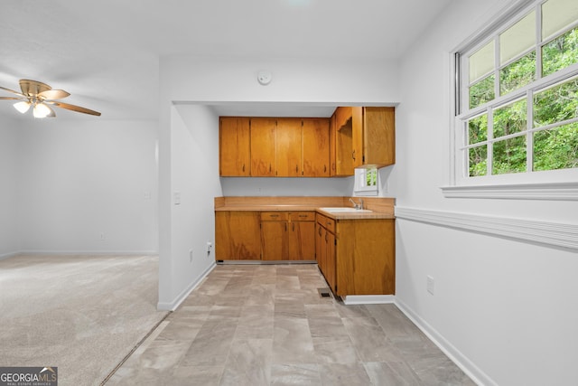 kitchen featuring brown cabinets, light countertops, a sink, and baseboards