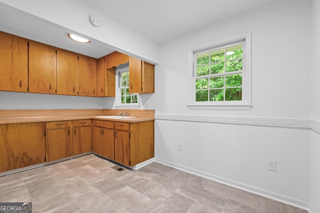 kitchen with light countertops, brown cabinetry, a sink, and baseboards