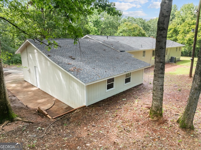 view of side of home featuring central AC and roof with shingles