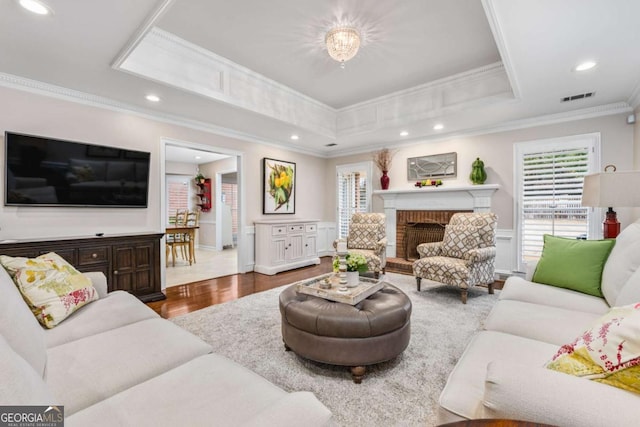 living room featuring visible vents, a raised ceiling, a wainscoted wall, crown molding, and a fireplace