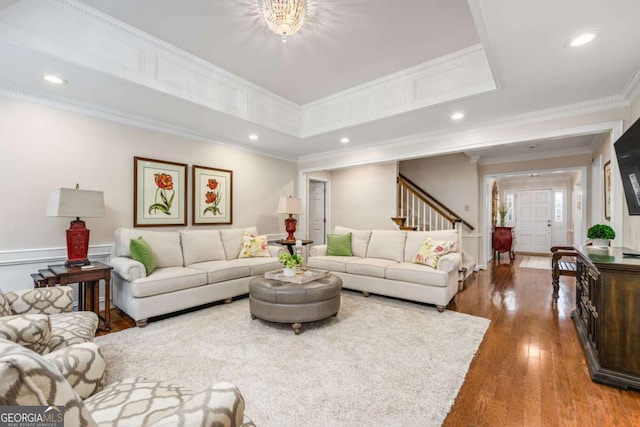 living room with recessed lighting, wood-type flooring, a raised ceiling, and crown molding