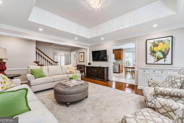 living room with crown molding, recessed lighting, a raised ceiling, wood finished floors, and stairs