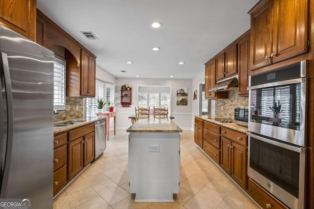 kitchen with light stone counters, a kitchen island, visible vents, baseboards, and appliances with stainless steel finishes