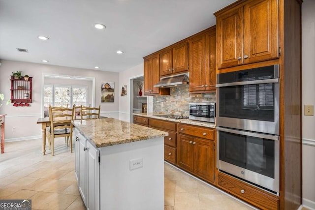 kitchen featuring tasteful backsplash, a kitchen island, light stone counters, stainless steel appliances, and under cabinet range hood