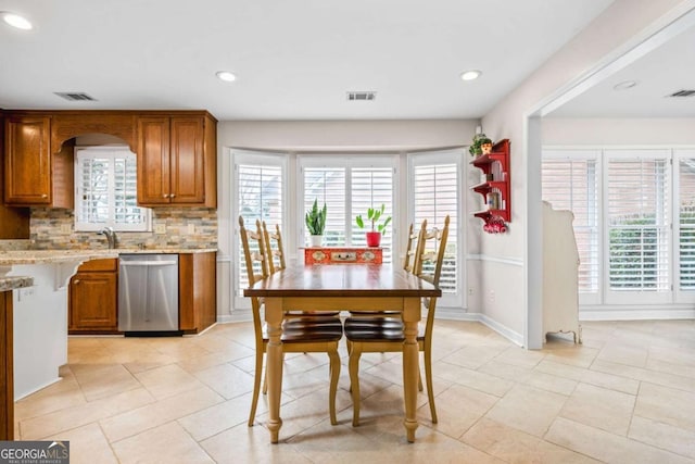 kitchen featuring visible vents, a healthy amount of sunlight, stainless steel dishwasher, decorative backsplash, and brown cabinetry