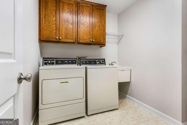 washroom featuring a sink, washing machine and clothes dryer, cabinet space, and baseboards