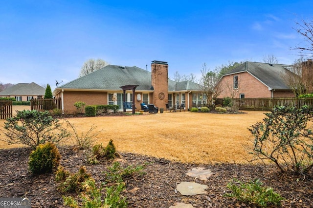 rear view of house with a patio, brick siding, fence, a lawn, and a chimney