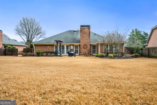 rear view of property featuring roof with shingles, brick siding, a yard, a chimney, and fence