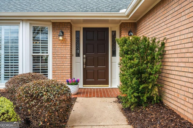 property entrance featuring roof with shingles and brick siding