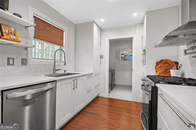 kitchen with dark wood-style flooring, tasteful backsplash, appliances with stainless steel finishes, a sink, and wall chimney range hood