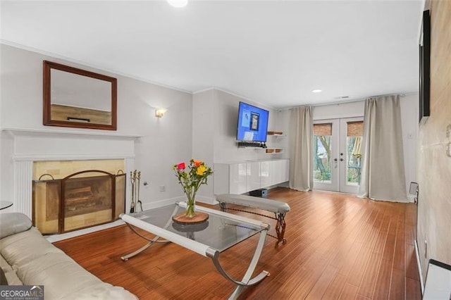 living room featuring french doors, a fireplace with flush hearth, ornamental molding, wood finished floors, and baseboards