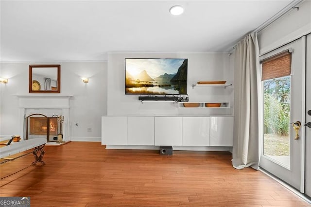 unfurnished living room featuring ornamental molding, a lit fireplace, light wood finished floors, and baseboards