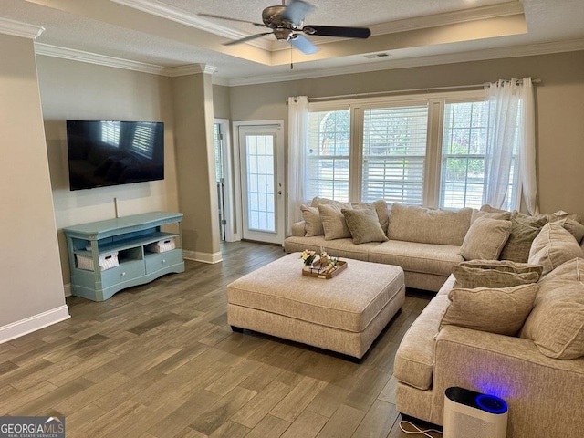 living room featuring visible vents, crown molding, a tray ceiling, and wood finished floors