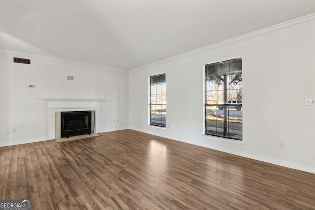 unfurnished living room with wood finished floors, a fireplace with flush hearth, visible vents, baseboards, and ornamental molding