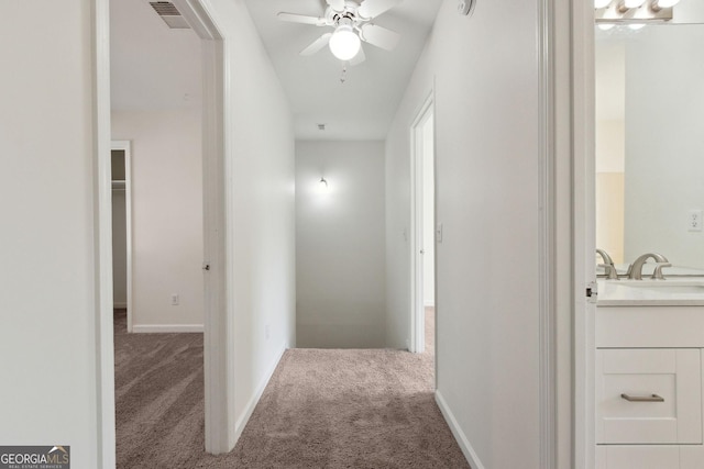 hallway featuring carpet flooring, a sink, visible vents, and baseboards