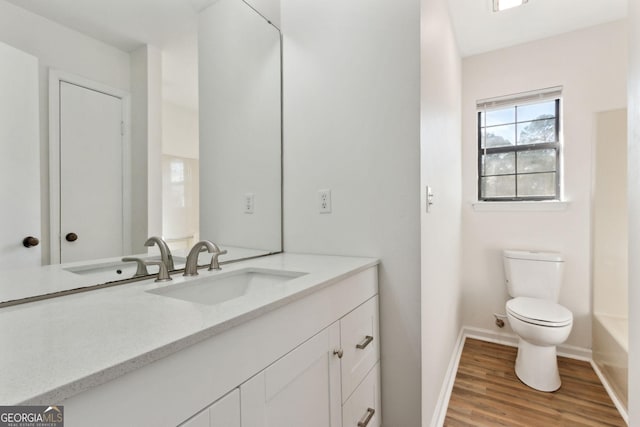 full bath featuring toilet, a washtub, wood finished floors, vanity, and baseboards