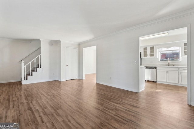 unfurnished living room with ornamental molding, a sink, wood finished floors, baseboards, and stairs