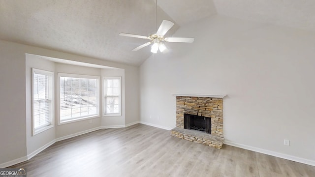 unfurnished living room with lofted ceiling, ceiling fan, wood finished floors, and a stone fireplace