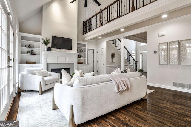 living room featuring dark wood finished floors, a fireplace, visible vents, stairway, and a towering ceiling