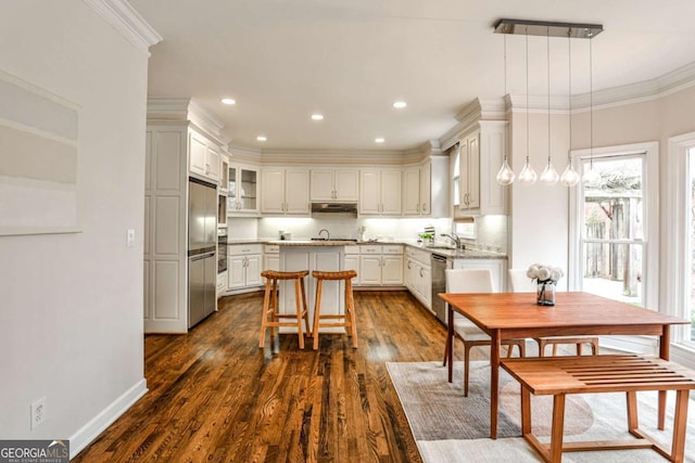 kitchen featuring dark wood-type flooring, a sink, ornamental molding, appliances with stainless steel finishes, and a center island