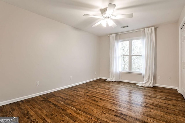 spare room with a ceiling fan, visible vents, dark wood finished floors, and baseboards