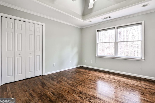 unfurnished bedroom featuring visible vents, baseboards, a raised ceiling, ornamental molding, and dark wood-style flooring