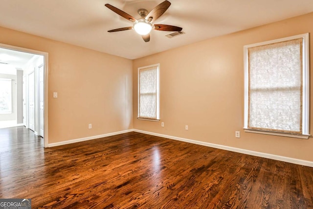 empty room featuring dark wood-type flooring, visible vents, baseboards, and a ceiling fan