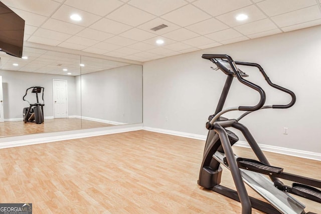 workout room with a paneled ceiling, wood finished floors, visible vents, and baseboards