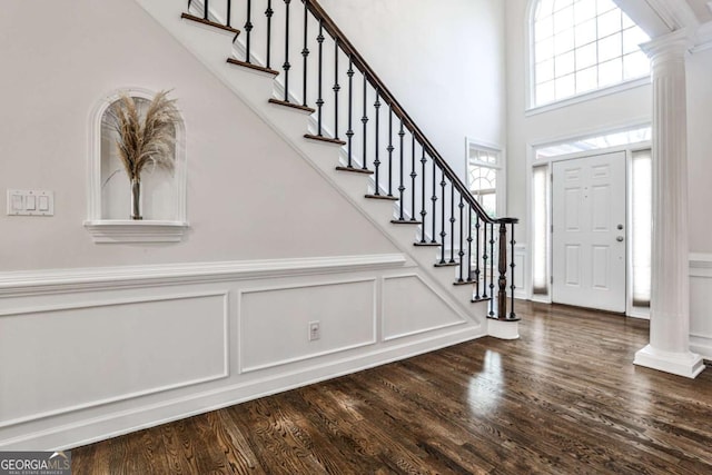 foyer entrance with stairs, decorative columns, a decorative wall, and wood finished floors