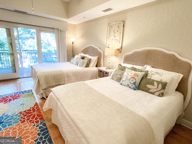 bedroom with a textured wall, access to outside, and wood finished floors