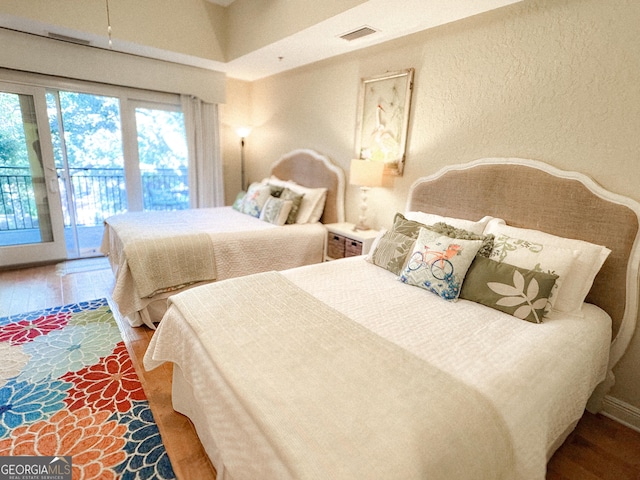 bedroom featuring access to outside, wood finished floors, visible vents, and a textured wall