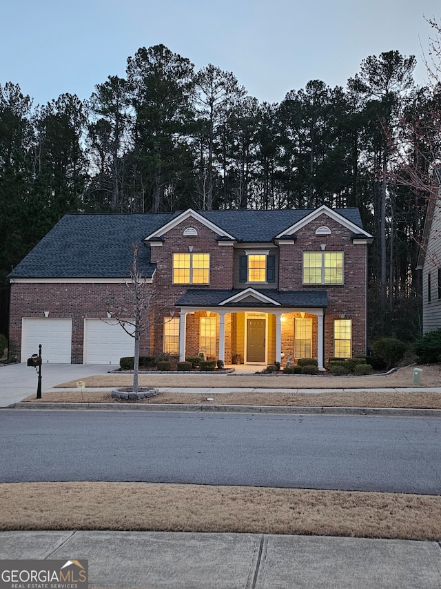 traditional-style house featuring a garage, driveway, brick siding, and a shingled roof