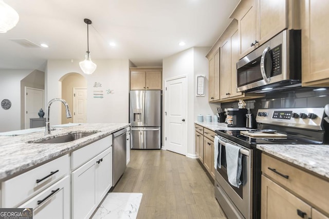 kitchen featuring appliances with stainless steel finishes, hanging light fixtures, light stone countertops, light wood-style floors, and a sink