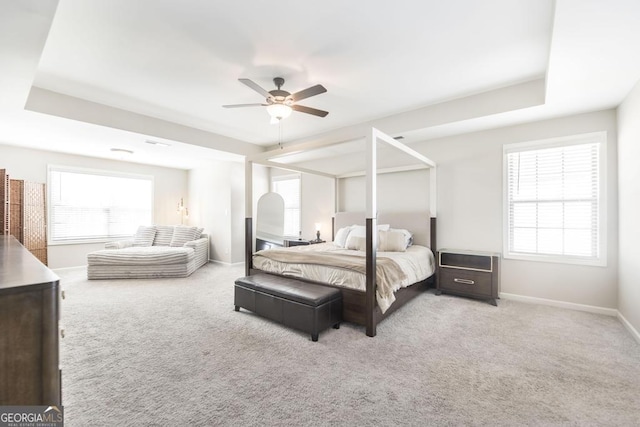 carpeted bedroom with a ceiling fan, a tray ceiling, and baseboards