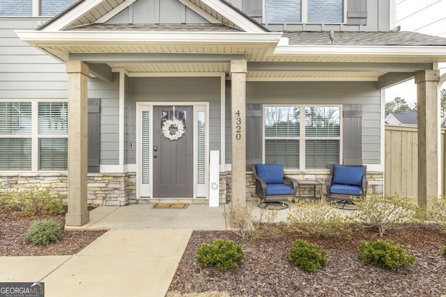 property entrance with a shingled roof, stone siding, fence, a porch, and board and batten siding