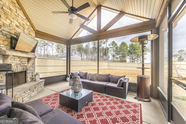 sunroom featuring a ceiling fan, vaulted ceiling, a wealth of natural light, and an outdoor stone fireplace