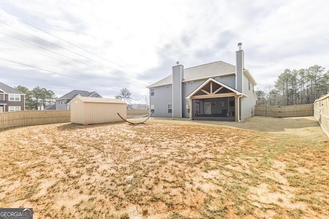 back of property featuring a chimney, a sunroom, a shed, a fenced backyard, and an outdoor structure