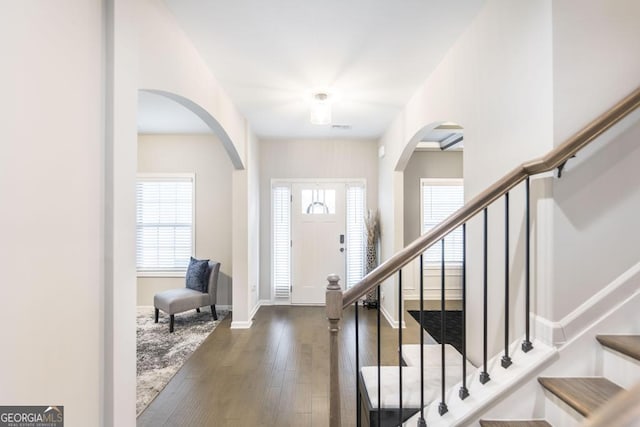 foyer with a wealth of natural light, dark wood finished floors, stairway, and baseboards