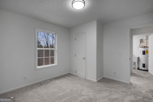 unfurnished bedroom featuring carpet, electric water heater, visible vents, and baseboards