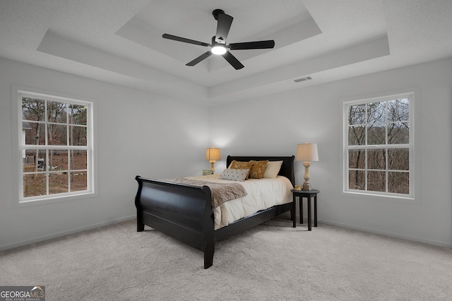 carpeted bedroom with visible vents, a tray ceiling, ceiling fan, and baseboards