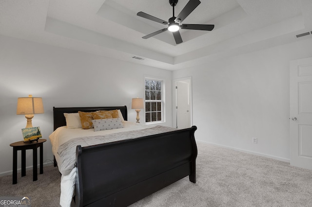 carpeted bedroom featuring visible vents, a tray ceiling, and baseboards