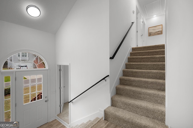 stairs featuring a towering ceiling, wood finished floors, and attic access