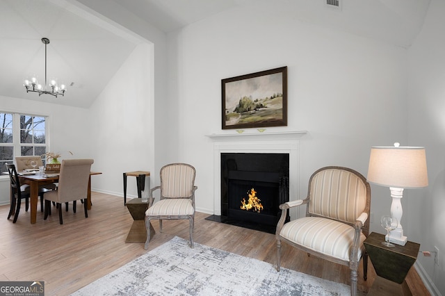 sitting room featuring a notable chandelier, vaulted ceiling, wood finished floors, a warm lit fireplace, and baseboards