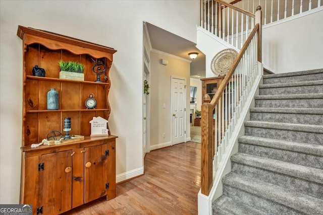 stairway with ornamental molding, wood finished floors, and baseboards