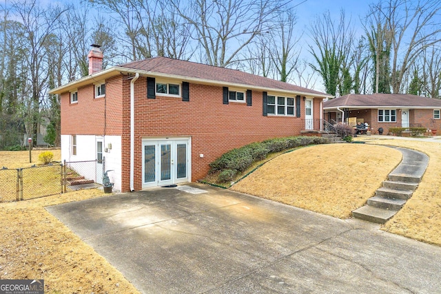 ranch-style house with a chimney, a gate, fence, french doors, and brick siding