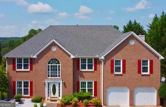 colonial house featuring an attached garage, brick siding, driveway, and a chimney