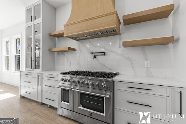 kitchen with range with two ovens, open shelves, light wood-style flooring, glass insert cabinets, and premium range hood