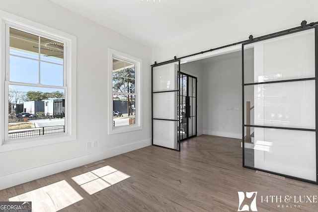 empty room featuring baseboards, a barn door, visible vents, and wood finished floors